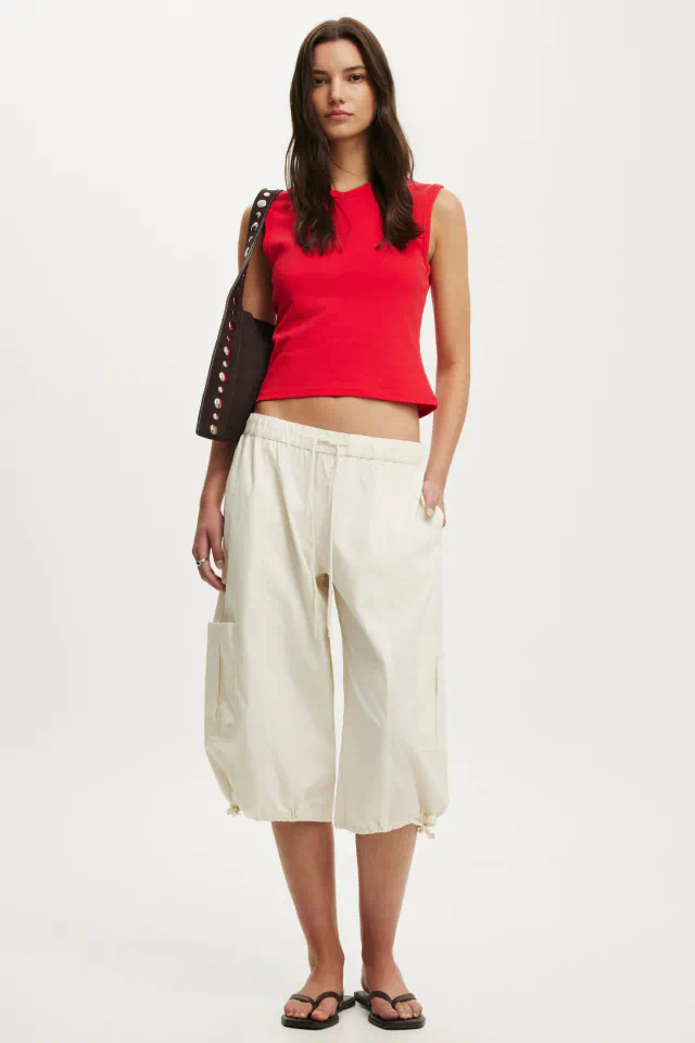 Woman wearing bright red sleeveless crop top and cream cargo pants with black studded shoulder bag and black slides