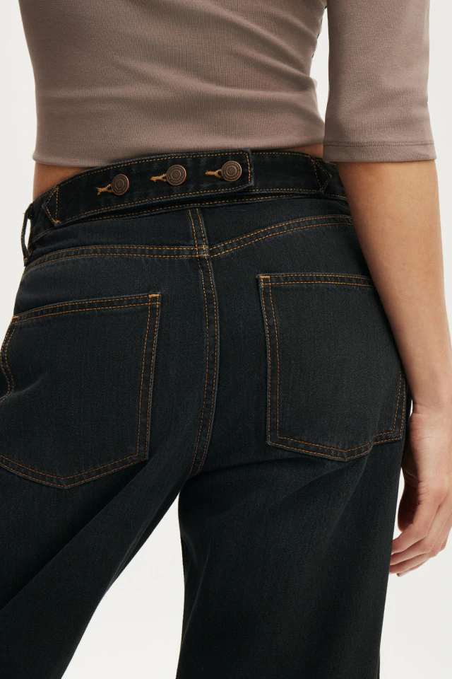 Person wearing dark denim jeans with contrast stitching and a black belt with decorative buckles, paired with a taupe ribbed long-sleeve top