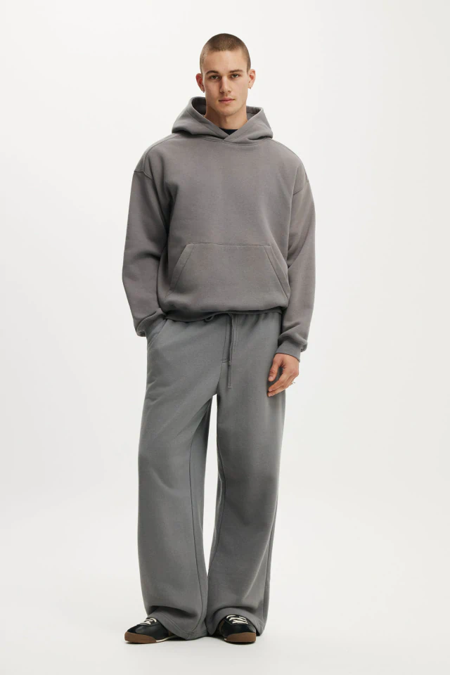 Male model wearing a gray hoodie and gray sweatpants with black slide sandals against a white background