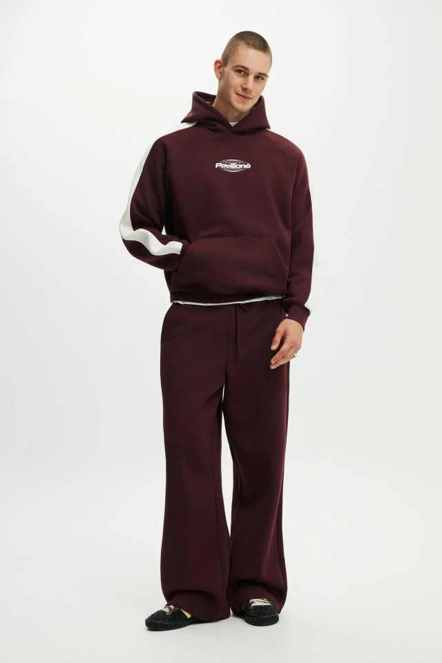 Male model wearing burgundy hoodie with white stripe and matching wide-leg sweatpants against white background