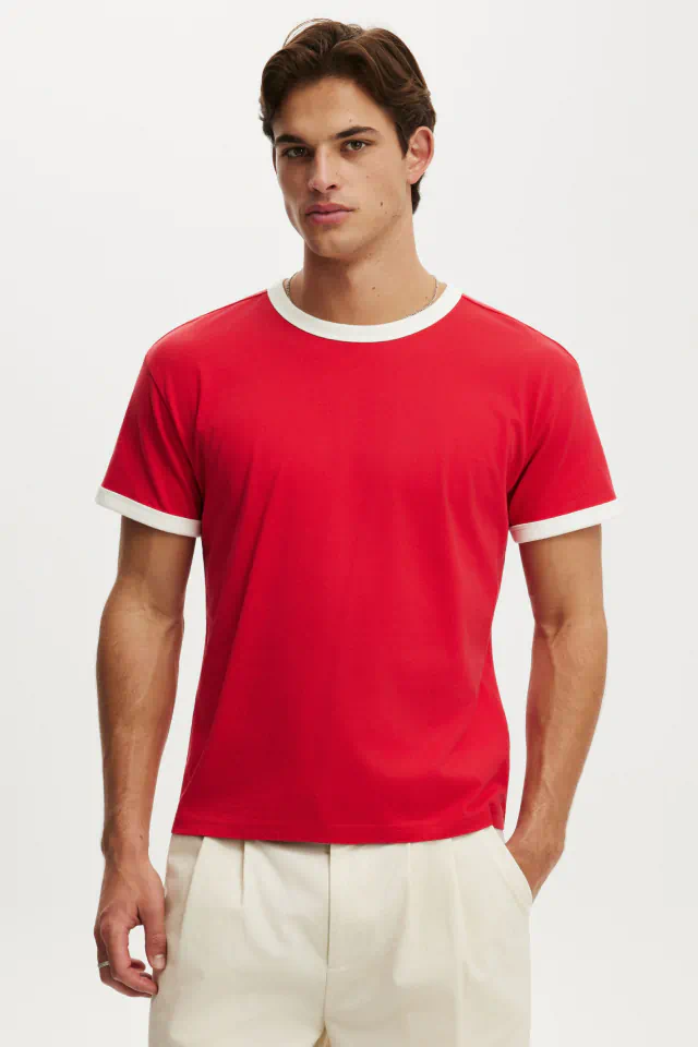 Man wearing red t-shirt with white collar and sleeve trim, paired with cream-colored pants, against white background