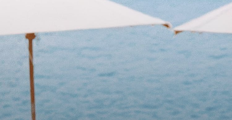 White umbrella against blue ocean and sky, with rust-colored pole visible on left side