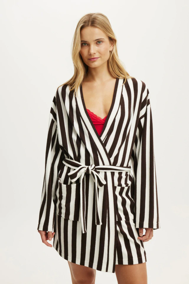 Woman wearing black and white striped wrap dress with long sleeves over red camisole against white background