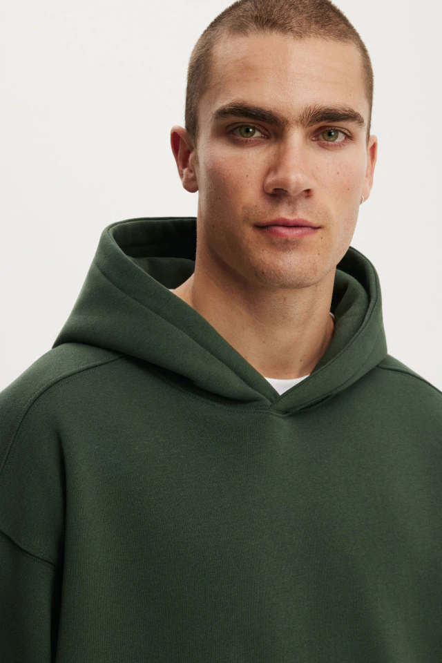 Young man wearing a dark green hoodie with a white undershirt, posed against a white background