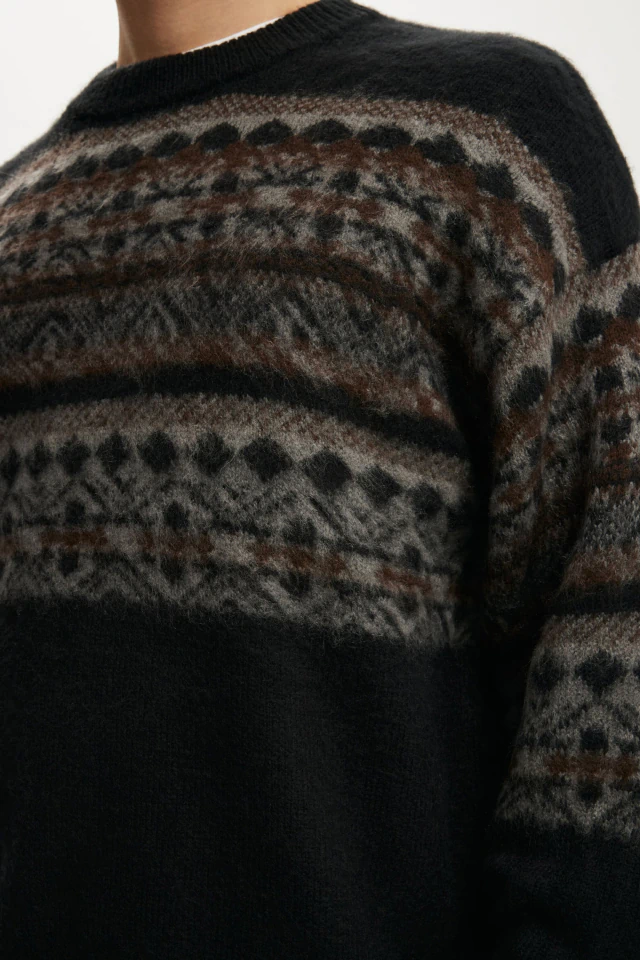 Close-up of a person wearing a black and brown patterned knit sweater with geometric designs on the chest and sleeves