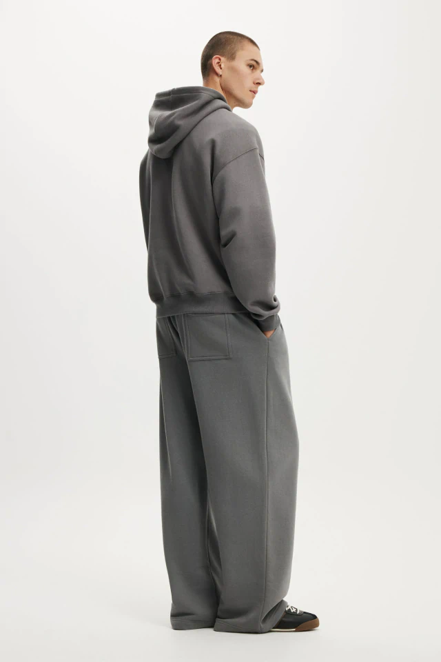 Man wearing charcoal grey hoodie and matching oversized sweatpants, standing in profile against a white background