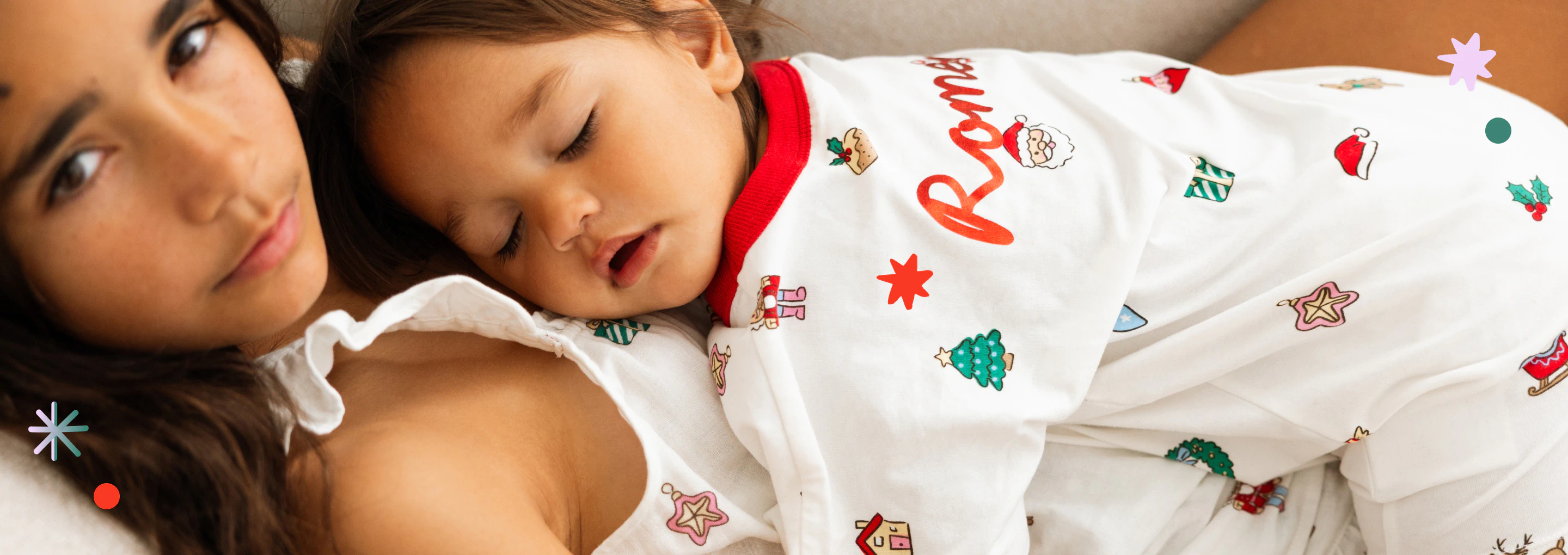 Adult and child sleeping together, child wearing white long-sleeve top with red trim and colorful holiday-themed print