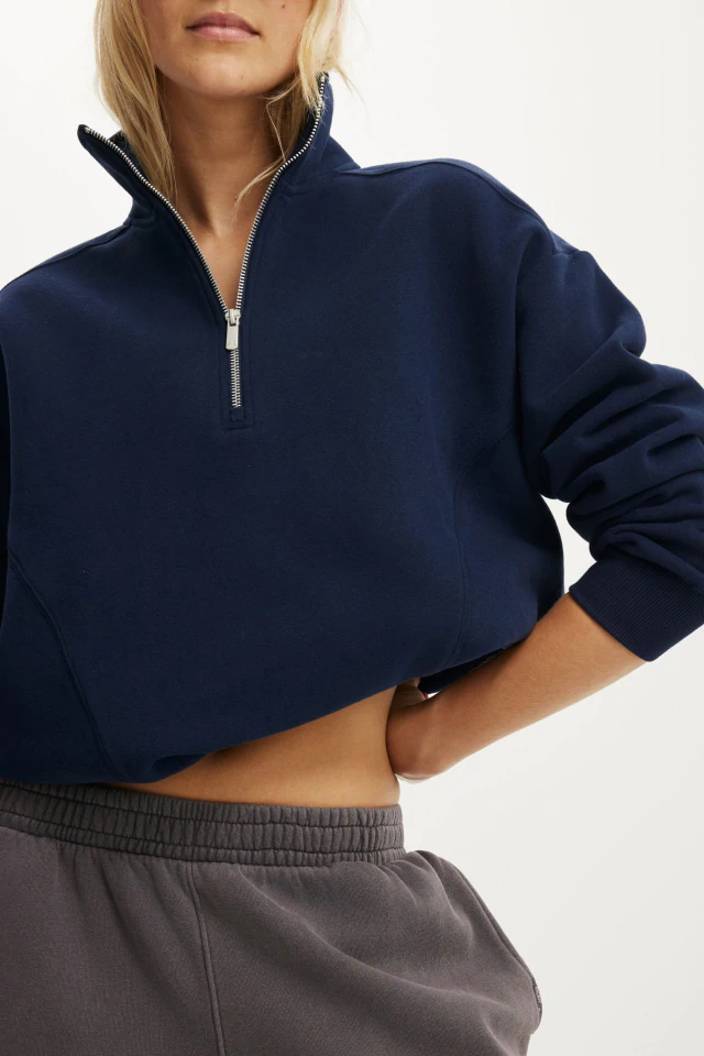 Woman wearing navy cropped half-zip sweatshirt and gray sweatpants against white background