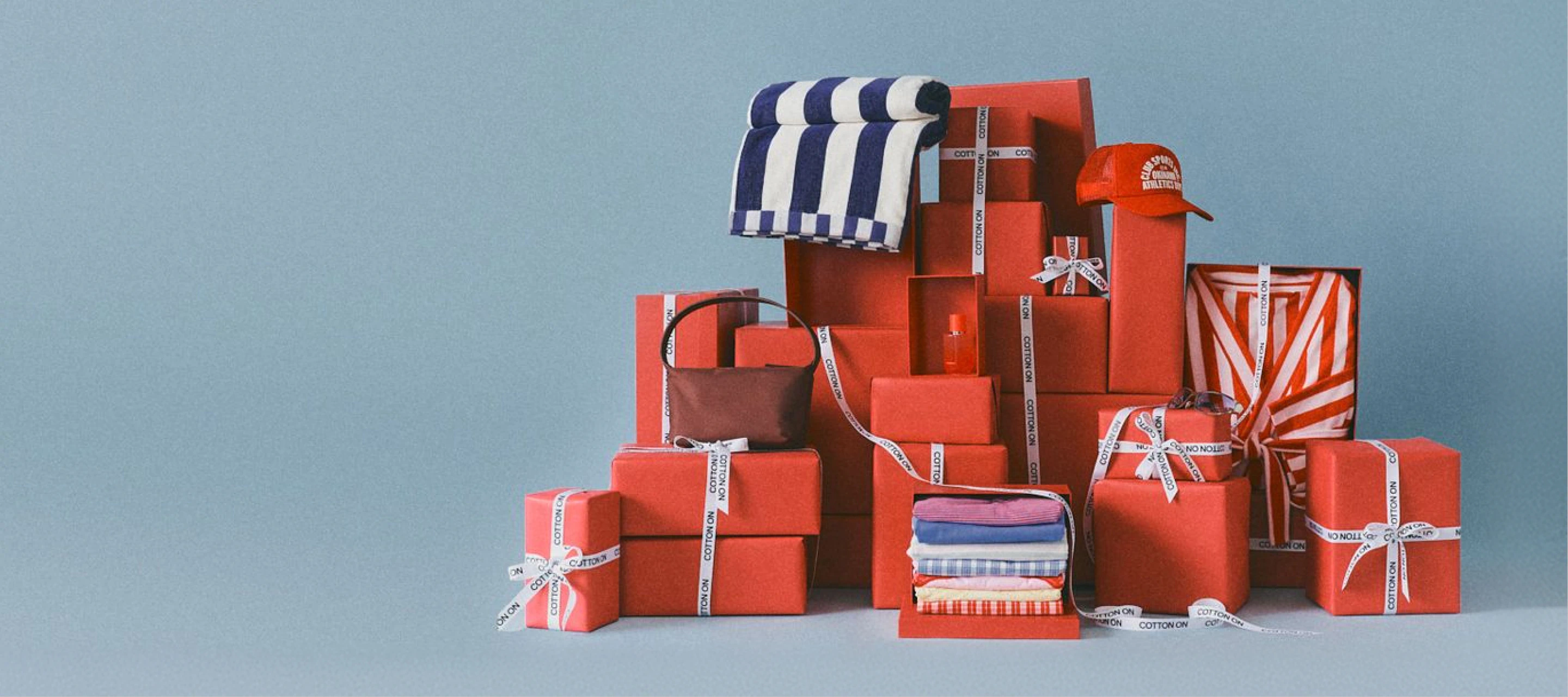 Cotton On branded red gift boxes arranged in a display with navy and white striped towel, folded colorful textiles, and an orange cap