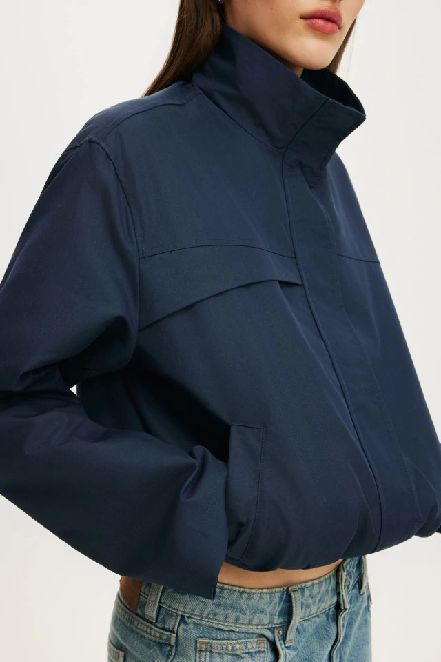 Woman wearing a cropped navy blue puffer jacket with a high collar, paired with light blue denim jeans