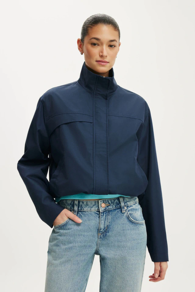 Woman wearing a navy cropped zip-up jacket over light blue jeans against a white background