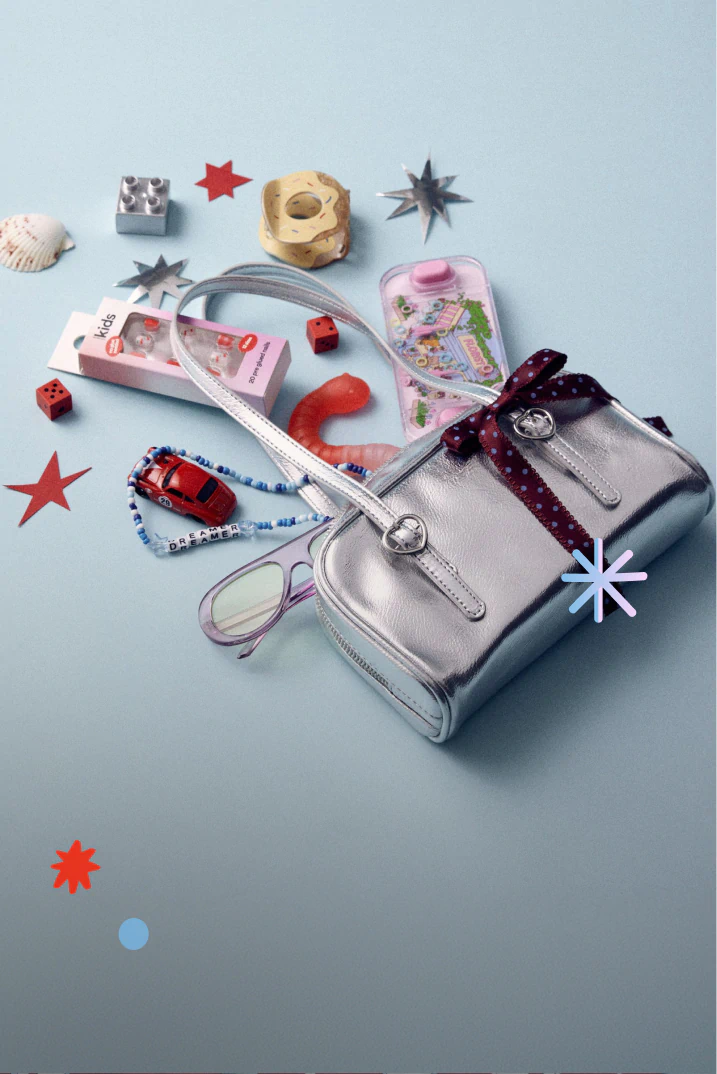 Silver metallic bag surrounded by colorful accessories including glasses, beaded bracelets, toy car, and decorative stars on blue background