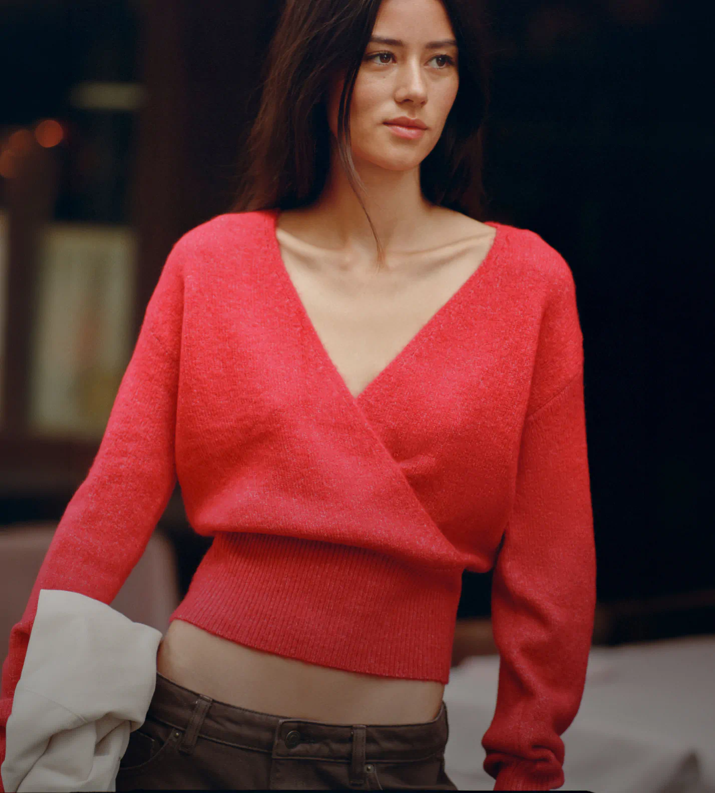 Woman wearing a bright red wrap-style knit sweater with ribbed waistband and cream-colored cuffs, paired with dark trousers