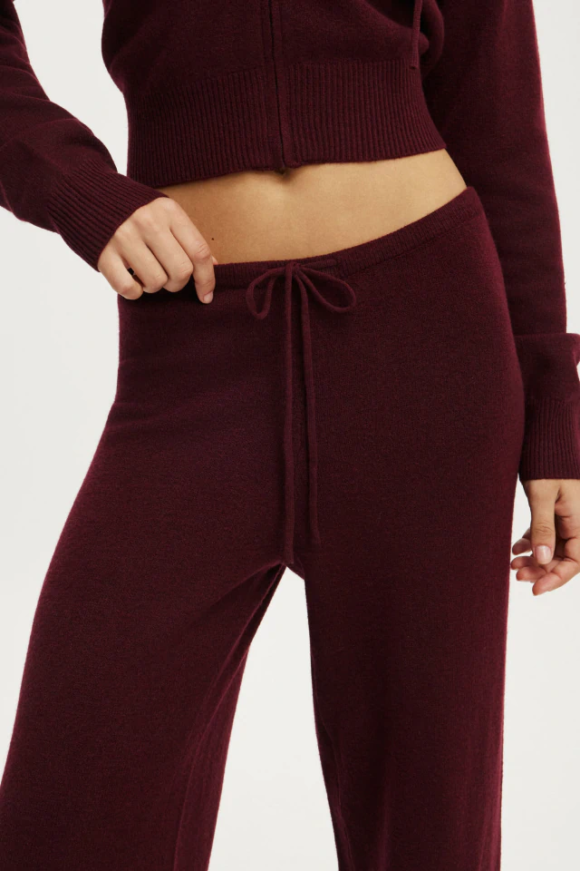 Woman wearing maroon knit crop top and matching drawstring pants against white background