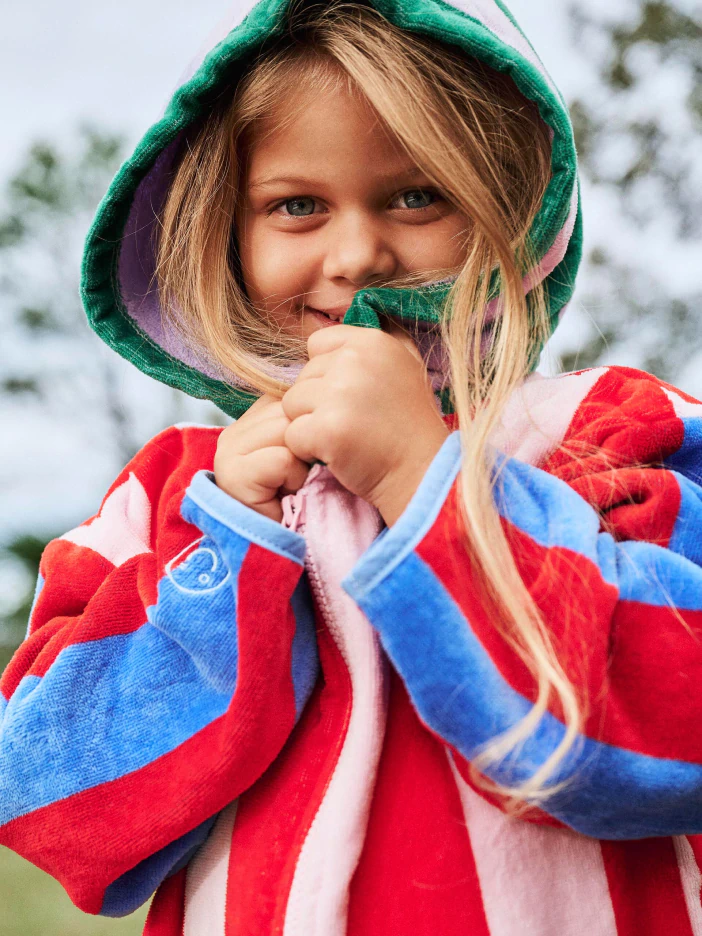Young child wearing a red and blue striped hoodie with green hood, smiling outdoors
