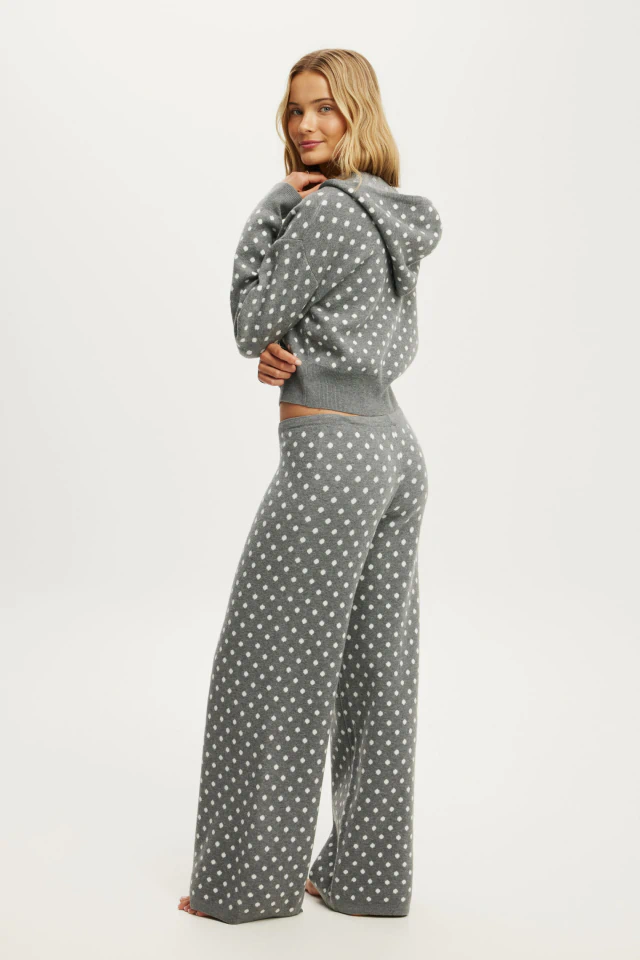 Woman wearing gray and white polka dot knit hoodie and matching wide-leg pants, standing against white background