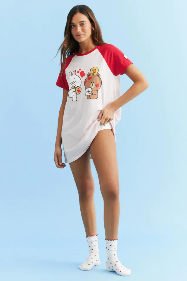 Young woman wearing white and red raglan t-shirt with cartoon characters and hearts, paired with white socks featuring small colorful patterns, standing against light blue background