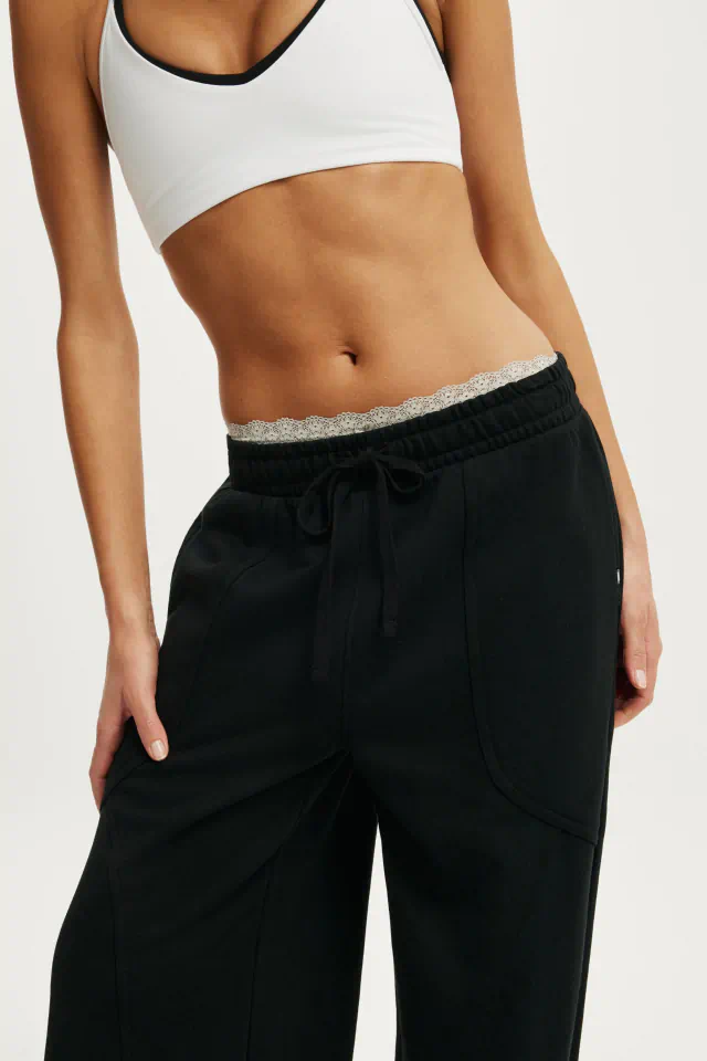 Woman wearing white sports bra and black drawstring pants with metallic waistband detail against neutral background