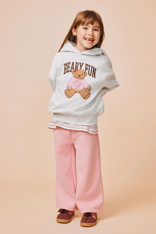 Young girl wearing cream cardigan with burgundy heart pattern and striped trim, smiling against light gray background