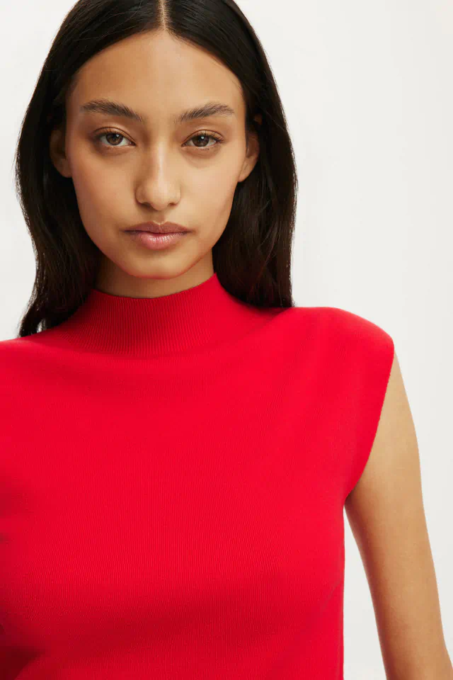 Woman with long black hair wearing a bright red sleeveless ribbed turtleneck against a white background
