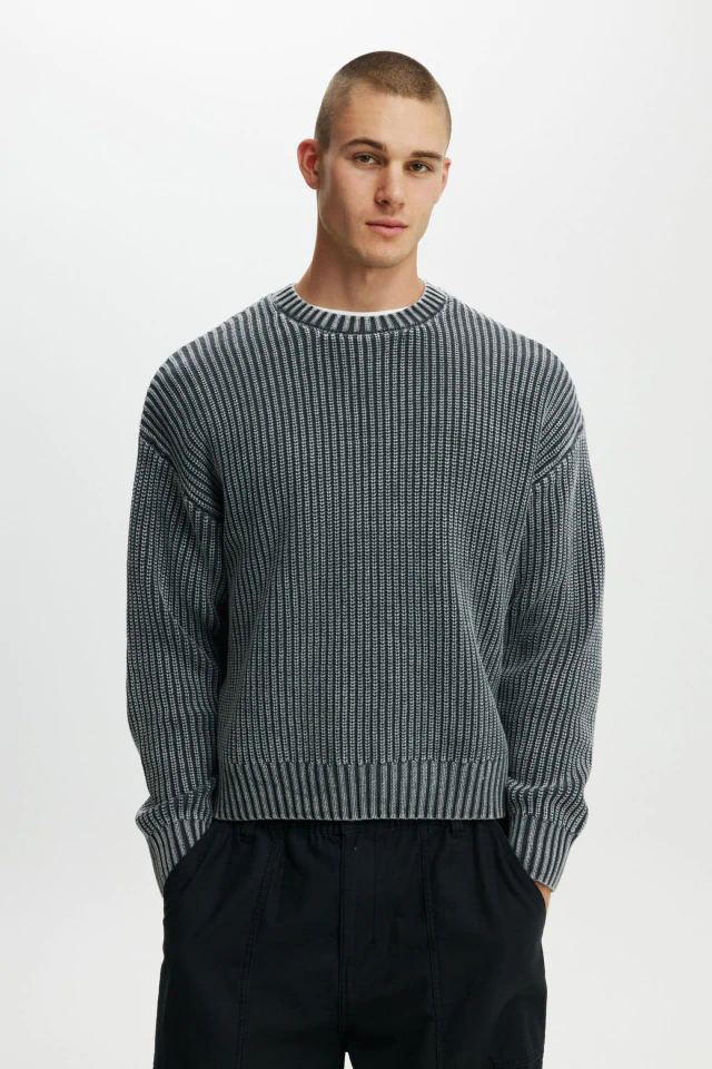 Male model wearing a grey ribbed knit crewneck sweater and black trousers against a white background