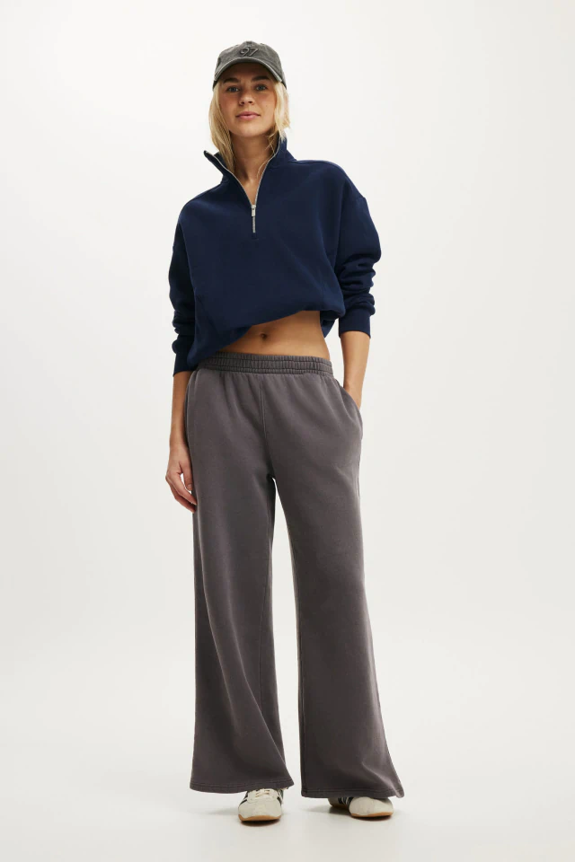 Woman wearing navy cropped quarter-zip sweatshirt, gray wide-leg sweatpants, and gray baseball cap against white background
