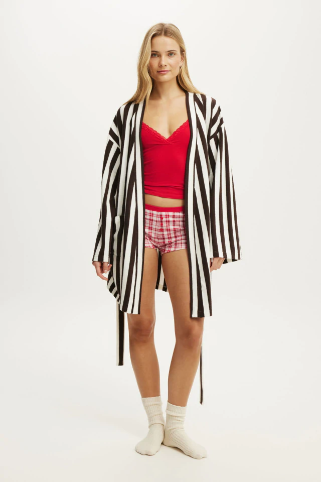 Woman wearing black and white striped cardigan over red crop top and red plaid shorts with white socks against white background