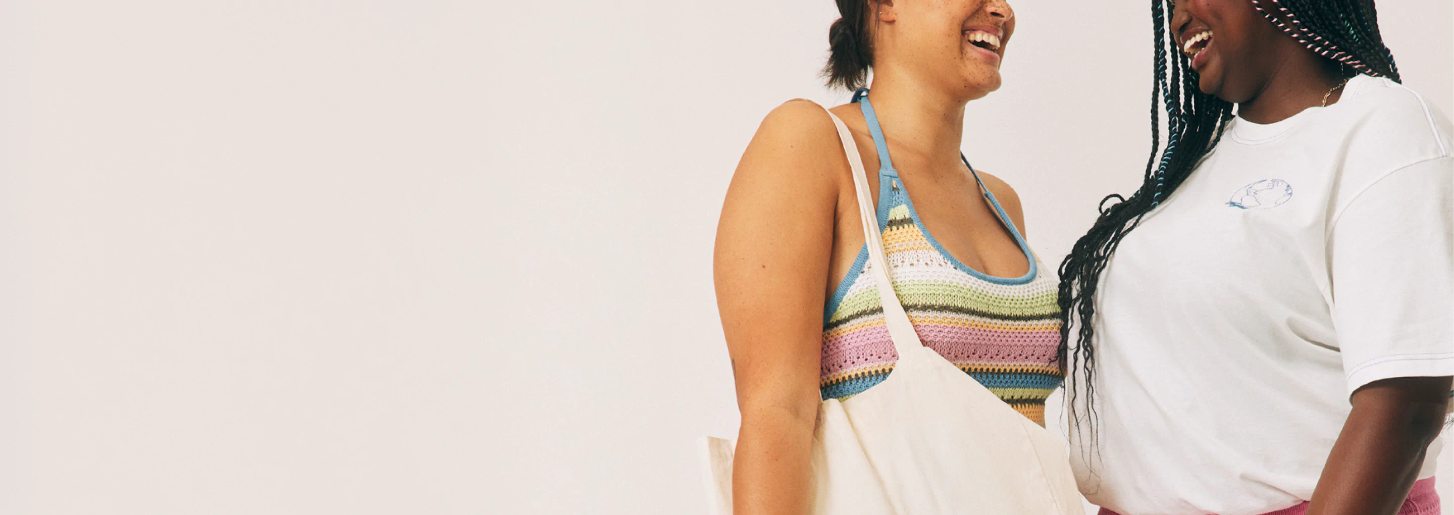 Two smiling people wearing casual summer clothing against a light background. One wears a colorful striped knit bikini top with a cream tote bag