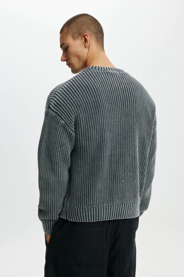Man wearing grey ribbed knit sweater and black pants, shown from behind against white background