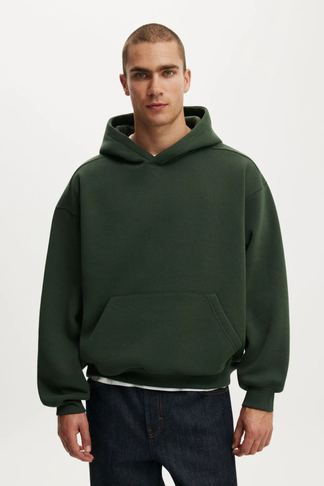 Man wearing dark green hoodie with kangaroo pocket and dark jeans against white background