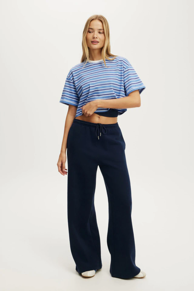 Woman wearing a blue and white striped cropped t-shirt and navy wide-leg sweatpants against a white background