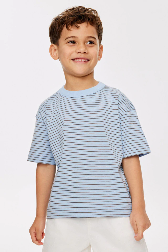 Three children smiling at camera wearing coordinating knit sweaters and jeans against white background
