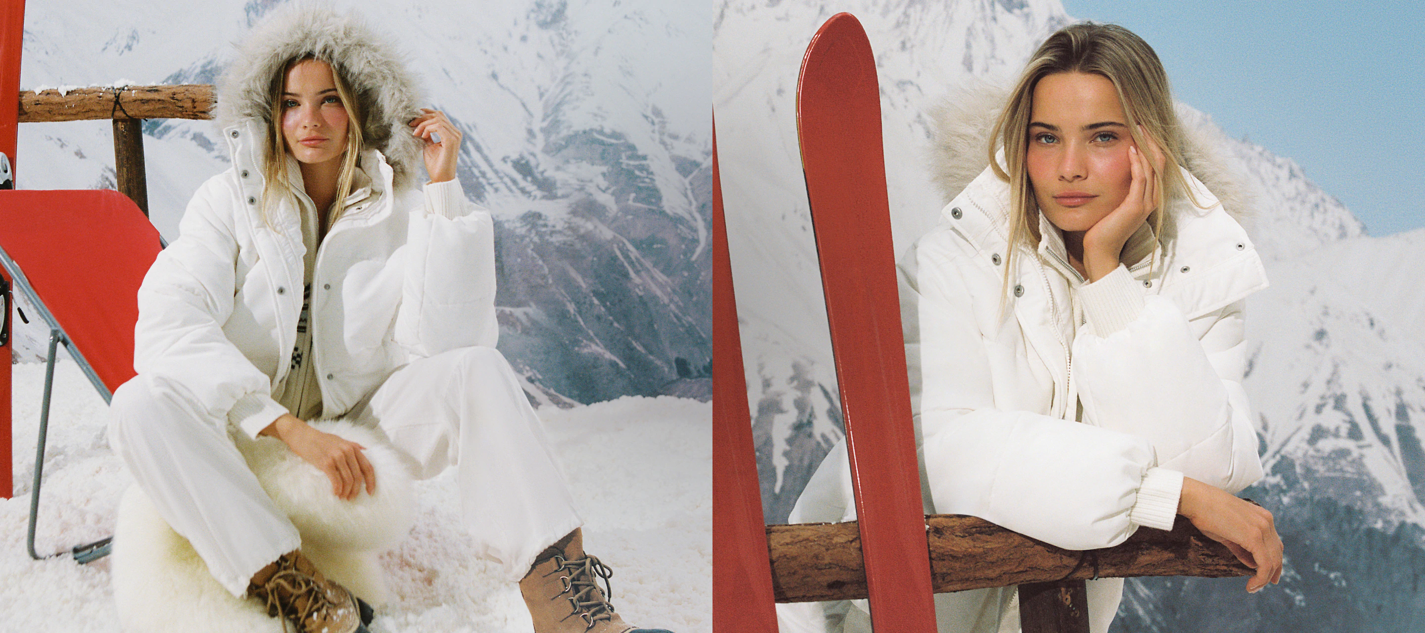 Two women wearing white puffer jackets pose against a snowy mountain backdrop with red skis and wooden ski equipment